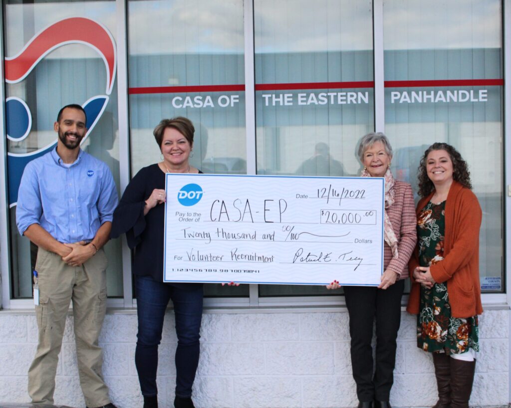 Four people stand outside a storefront holding a large ceremonial check representing a donation or business partnership.