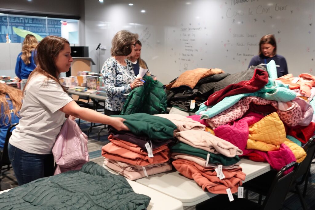 A group of volunteers organize and sort a large collection of donated clothing items at an indoor workshop or community center.