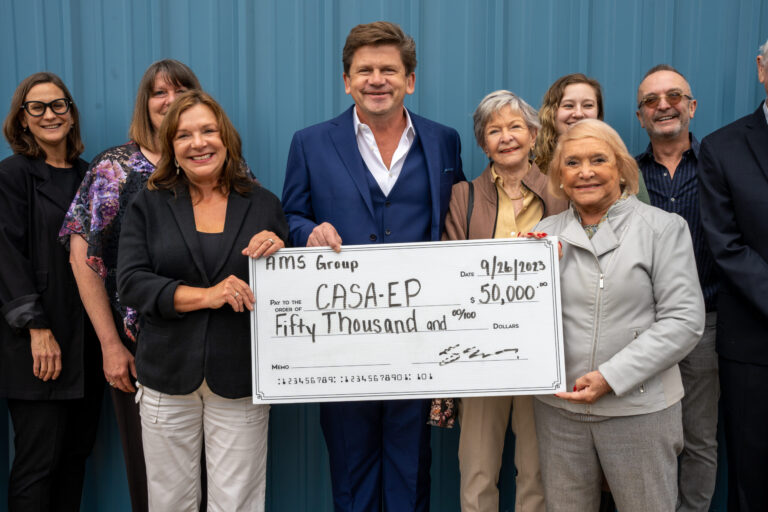 A group of eight people pose together while holding a large ceremonial check for fifty thousand dollars presented to CASAEP charity.