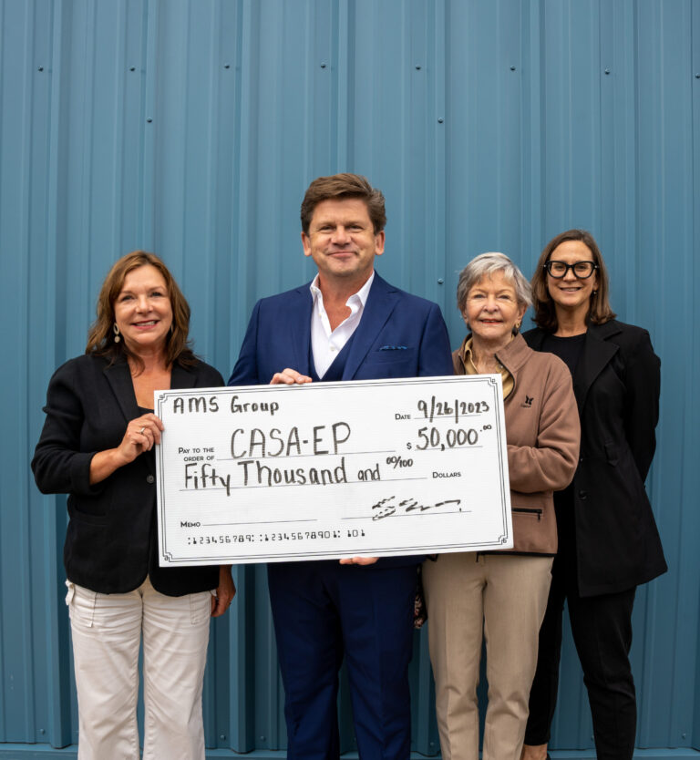 Four professionals proudly display a large ceremonial check for $50,000 donated to CASA-EP, standing in front of a blue corrugated metal backdrop.