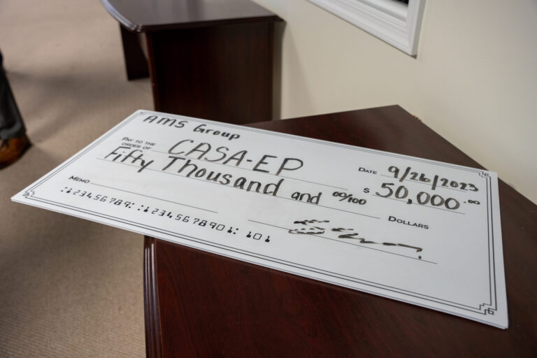 A large ceremonial check displayed on a wooden table during an auction or fundraising event, showing a significant monetary award.