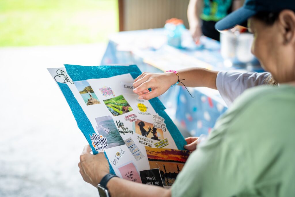 A person in a green shirt reads a blue brochure or pamphlet while others gather outdoors in a casual, daytime setting.