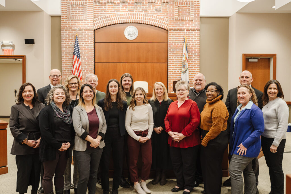 A formal group portrait of approximately 18 professional women posed together in front of a distinctive brick archway in an elegant indoor venue.