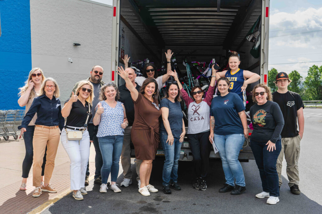 A large group of people pose together in front of an open delivery truck at a warehouse or loading dock, celebrating as a team.