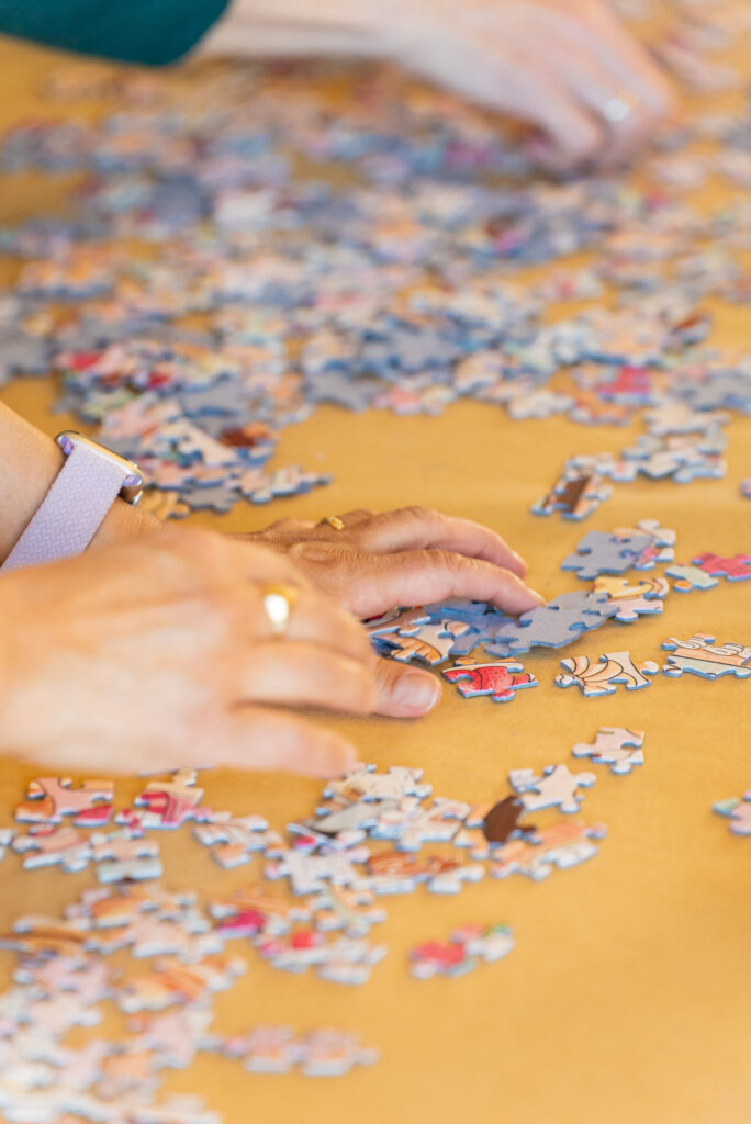 Close-up overhead view of hands assembling a colorful jigsaw puzzle on a golden-yellow work surface.