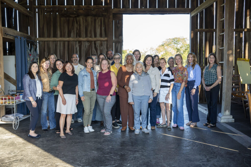 A large group of people posed together in front of an open barn doorway during daytime, suggesting a community event or organized gathering.