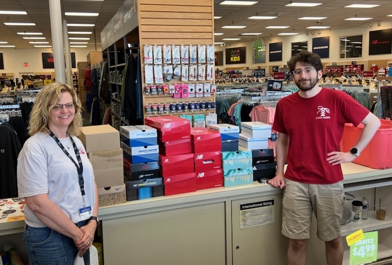 Two people stand at a counter in an indoor auction or retail venue with red bins and merchandise visible in the background.