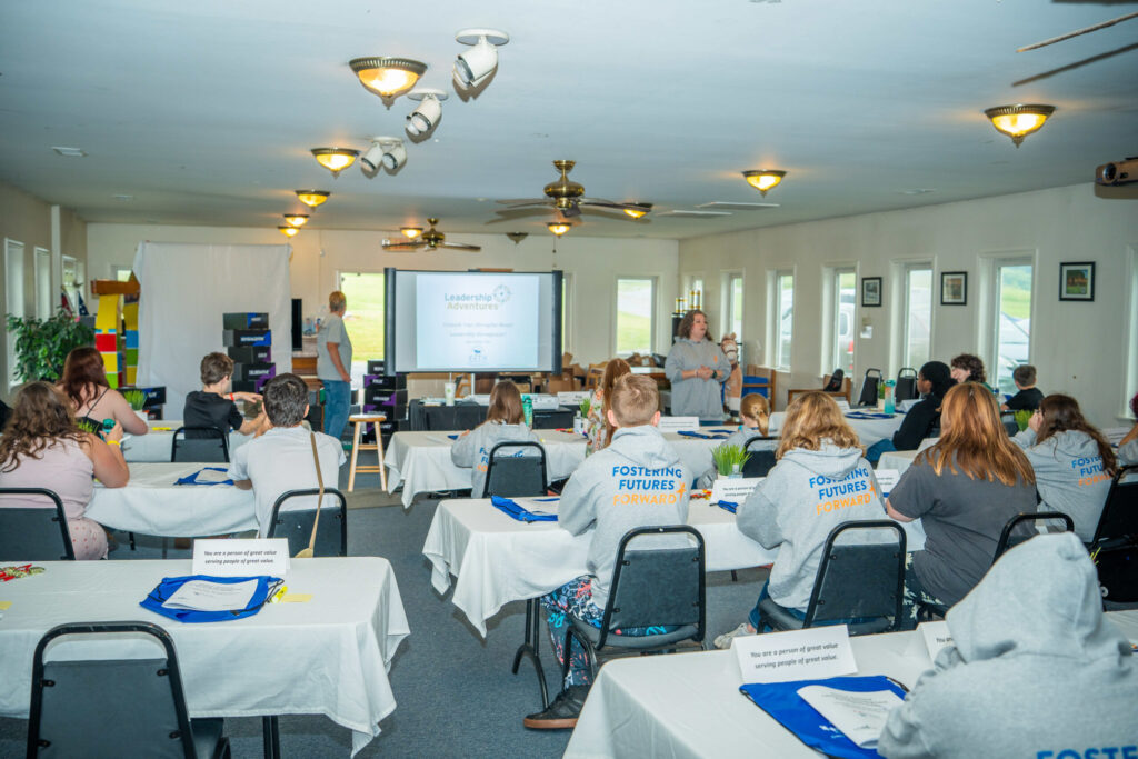 A group of participants seated at tables during an indoor workshop or training session in a bright, well-lit room with presentation equipment.