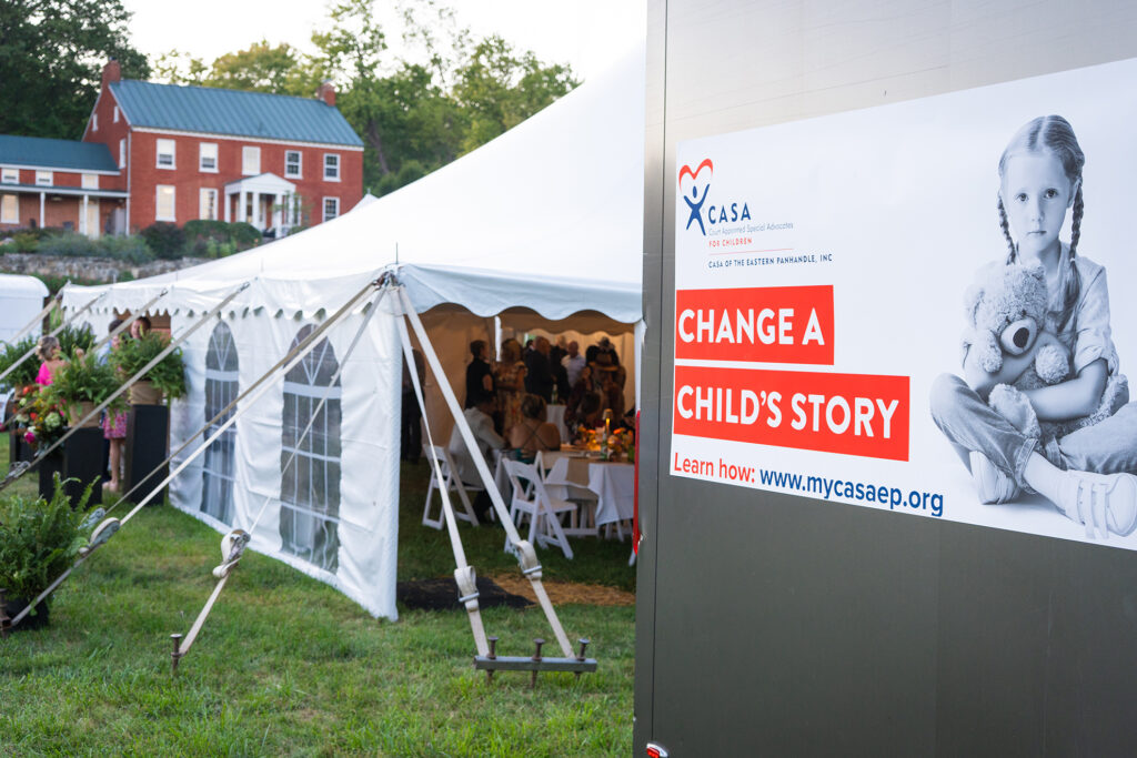 A white tent event venue set up outside a red barn with a fundraising banner promoting a children's charity campaign.