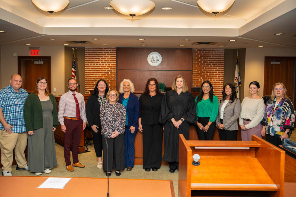 A formal group photo of approximately fifteen people posed together in what appears to be a courtroom or judicial chamber with wooden furnishings and professional lighting.