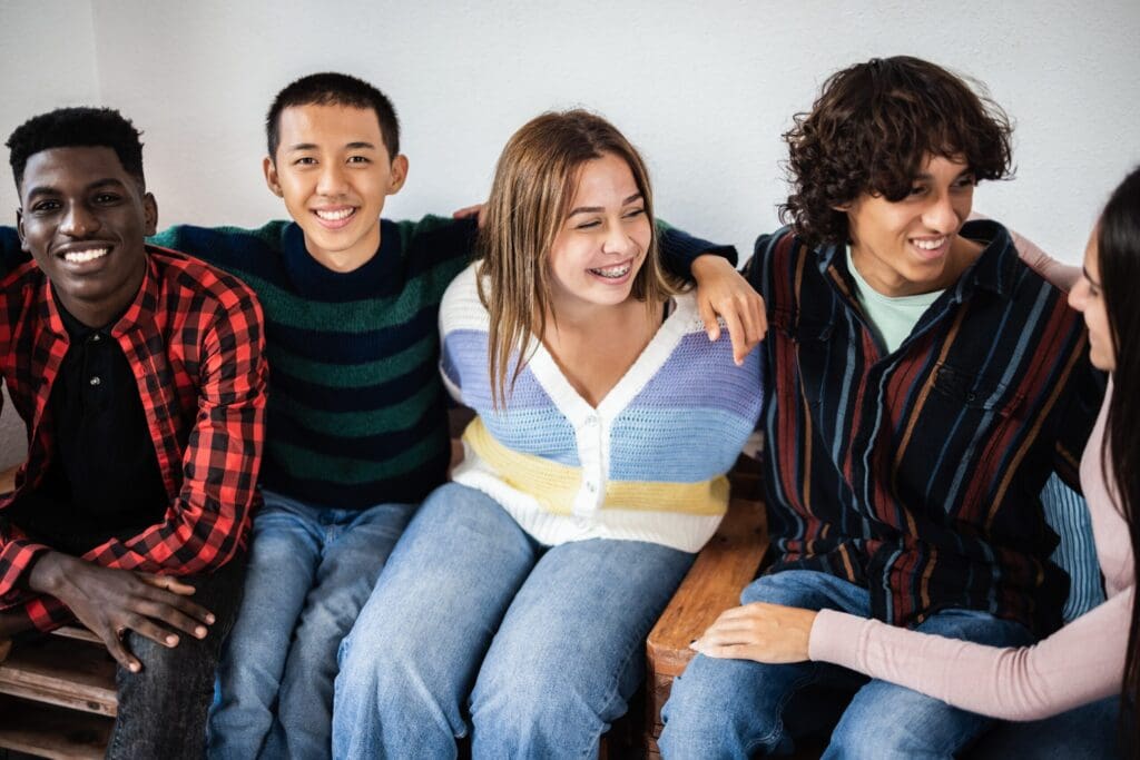 A diverse group of five young people pose together casually against a white background in a friendly, relaxed manner.